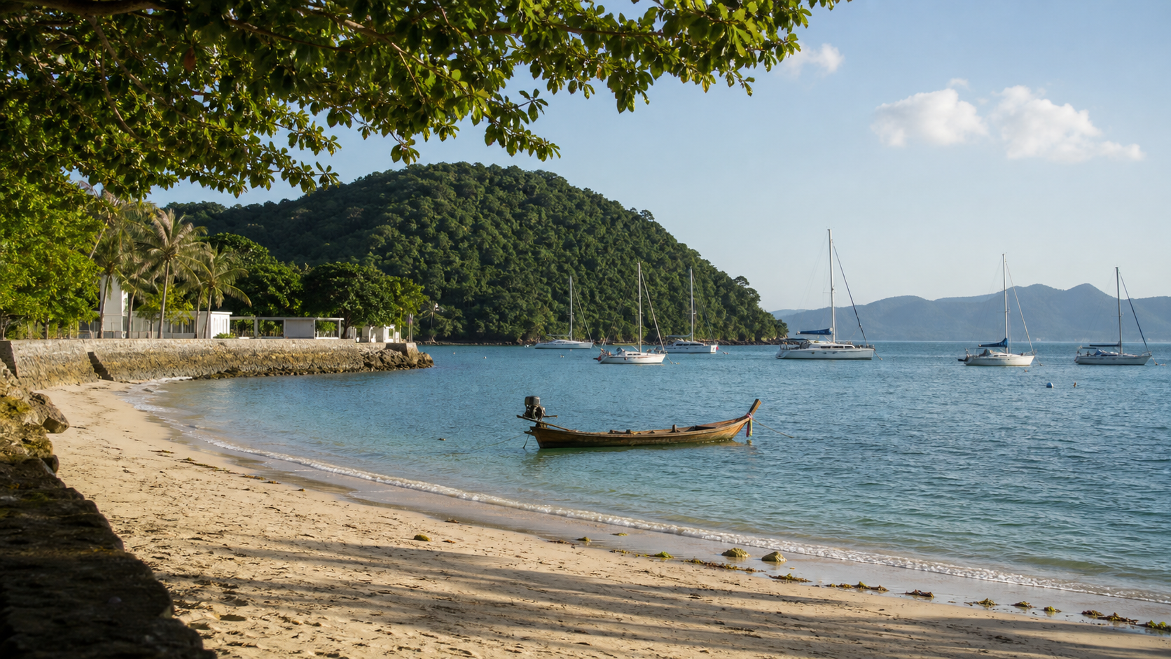 Longtail boats and small sailboats in the calm bay at Ao Yon Beach Phuket