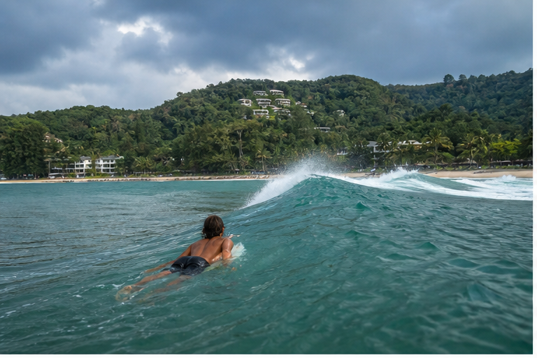A surfer paddling into a monsoon-season wave at Kata Beach in Phuket