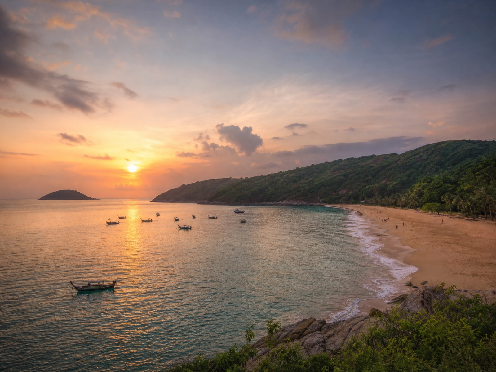 Nai Harn Beach at sunset with a curved bay, green hills, and calm water
