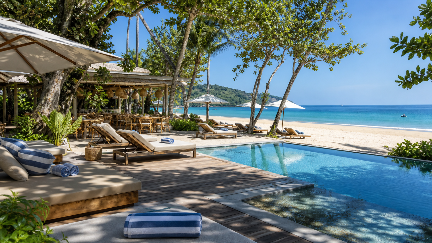 Relaxed daytime Phuket beach club with loungers, pool, shade, and sea view